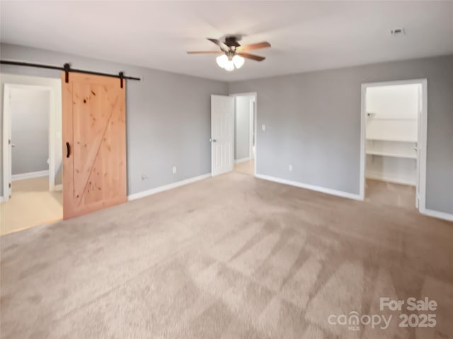 unfurnished bedroom with ceiling fan, carpet, a barn door, a walk in closet, and a closet