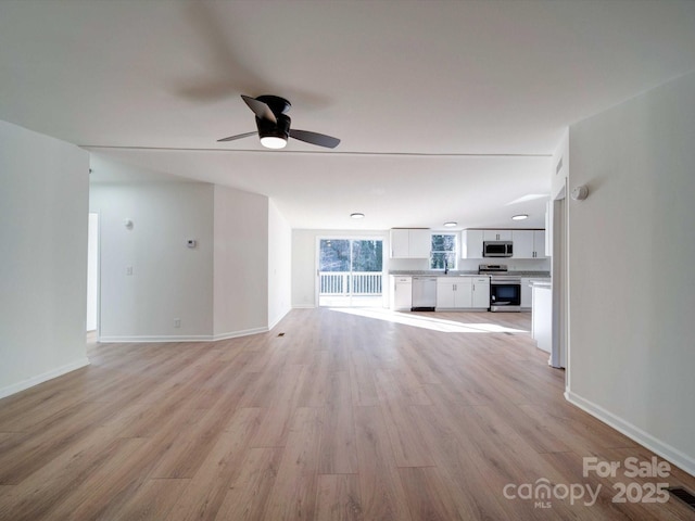 unfurnished living room with sink, ceiling fan, and light wood-type flooring