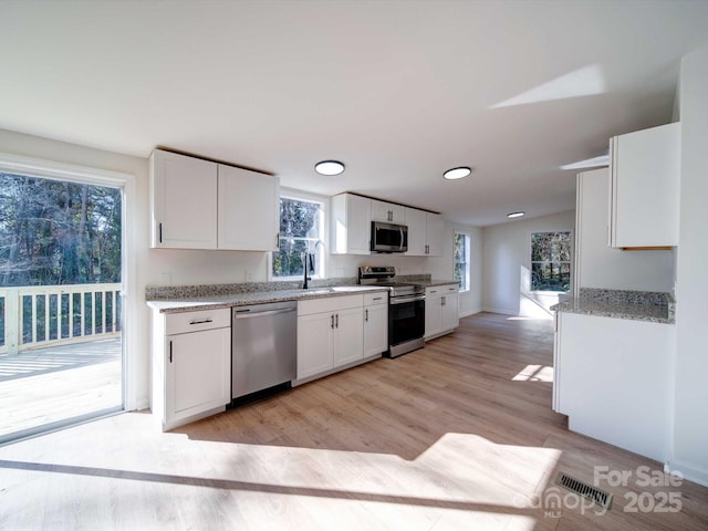 kitchen featuring sink, light hardwood / wood-style flooring, appliances with stainless steel finishes, light stone countertops, and white cabinets