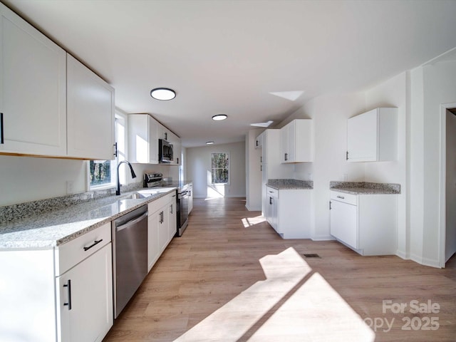 kitchen with stainless steel appliances, light stone countertops, light wood-type flooring, and white cabinets