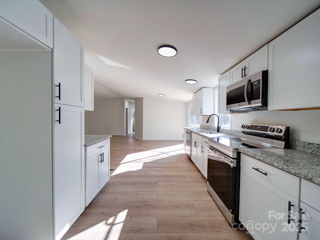 kitchen with light stone counters, appliances with stainless steel finishes, light hardwood / wood-style flooring, and white cabinets