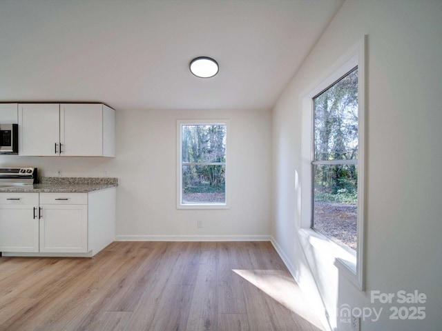 kitchen with white cabinetry, appliances with stainless steel finishes, light stone counters, and light hardwood / wood-style flooring