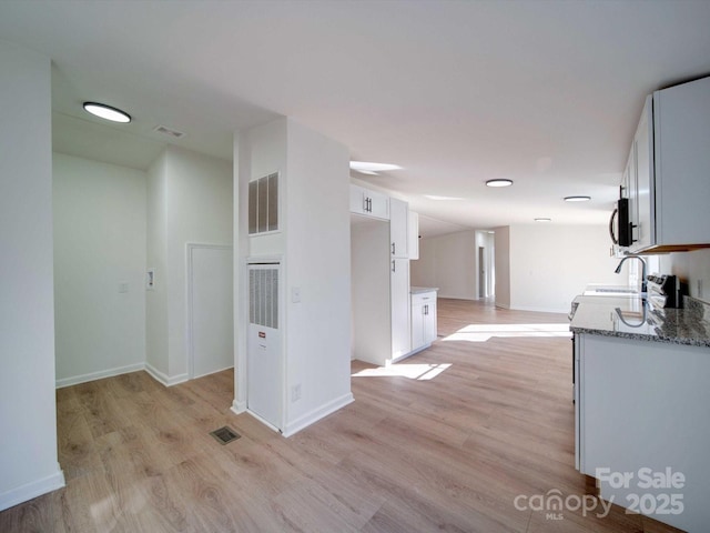 kitchen with white cabinetry, sink, light stone counters, and light hardwood / wood-style flooring