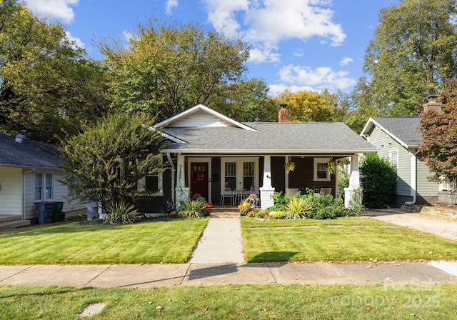 view of front of property featuring covered porch, a front lawn, a chimney, and a shingled roof