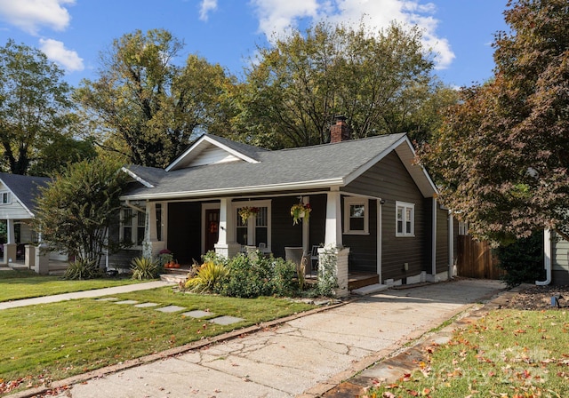 view of front of property with a porch, a shingled roof, concrete driveway, a front lawn, and a chimney