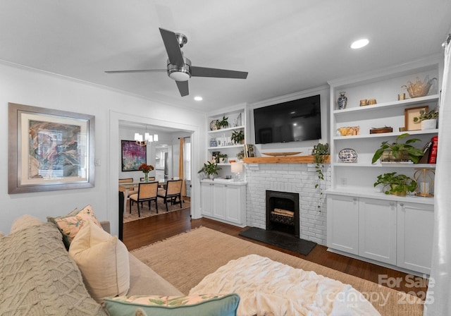 living area featuring recessed lighting, ceiling fan with notable chandelier, built in features, a brick fireplace, and dark wood-style floors