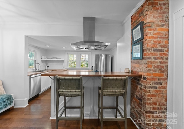 kitchen with a breakfast bar area, island range hood, stainless steel appliances, a peninsula, and wood counters