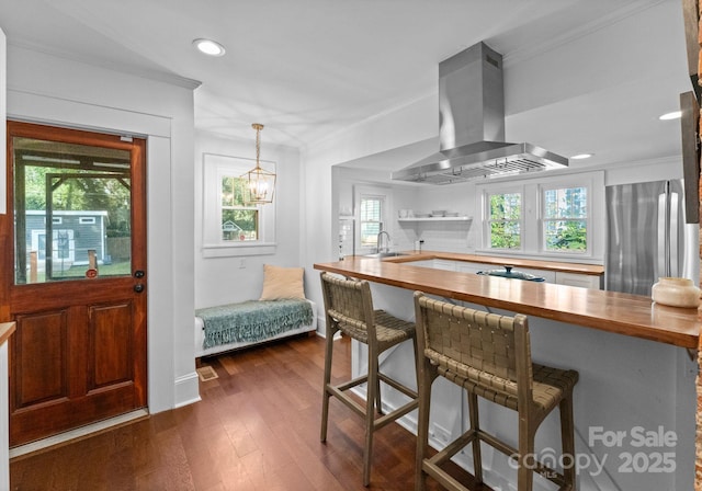 kitchen featuring a breakfast bar area, butcher block counters, freestanding refrigerator, dark wood-style floors, and island exhaust hood