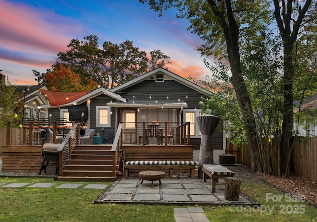 back of house at dusk with an outdoor fire pit, stairs, fence, a wooden deck, and a patio area