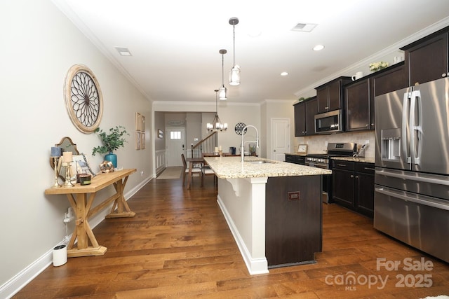 kitchen featuring appliances with stainless steel finishes, pendant lighting, sink, a kitchen island with sink, and light stone countertops