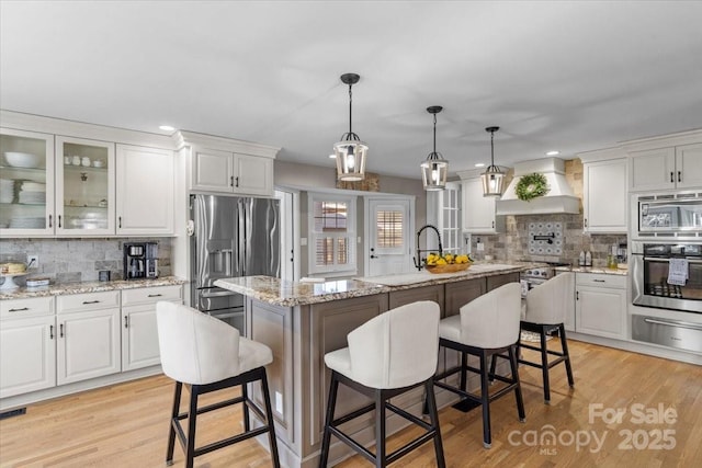 kitchen featuring premium range hood, a breakfast bar area, white cabinetry, a center island with sink, and appliances with stainless steel finishes