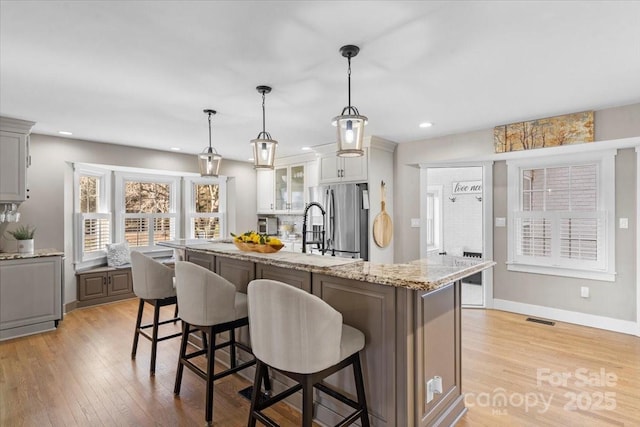 kitchen featuring hanging light fixtures, an island with sink, a kitchen bar, and stainless steel fridge with ice dispenser