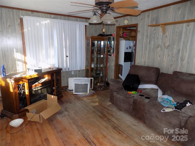 living room featuring crown molding, a wall mounted AC, hardwood / wood-style flooring, ceiling fan, and a fireplace