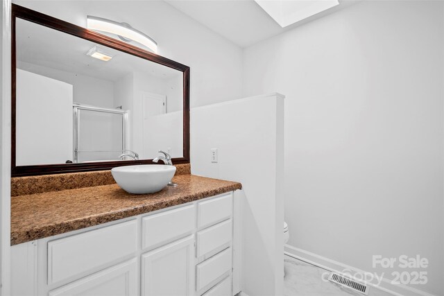 bathroom with vanity, toilet, a skylight, and a shower with shower door