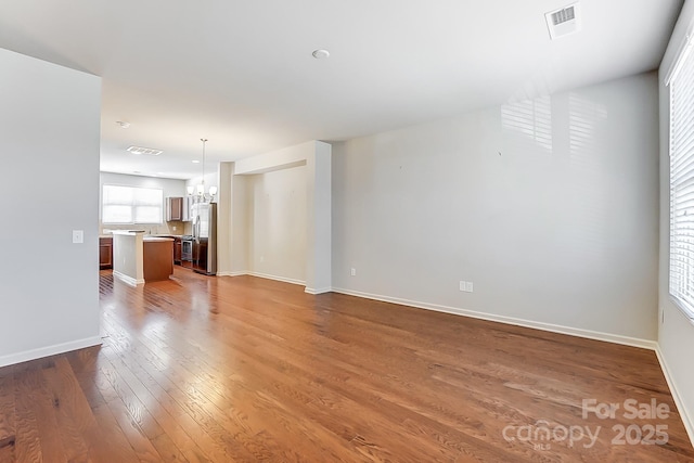 unfurnished living room featuring an inviting chandelier and dark hardwood / wood-style floors