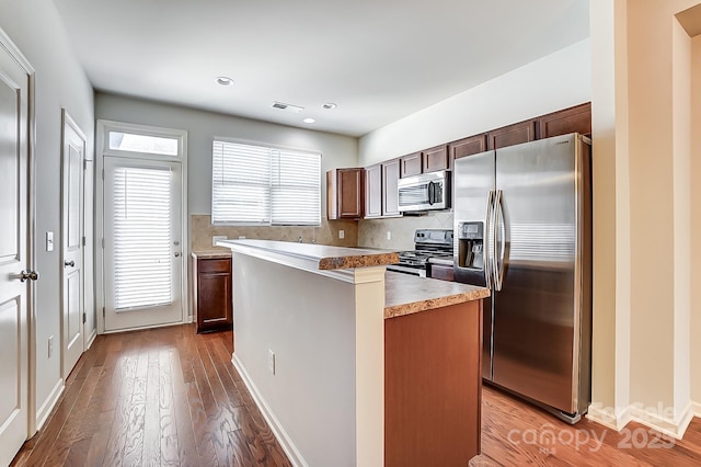 kitchen with decorative backsplash, wood-type flooring, stainless steel appliances, and a kitchen island