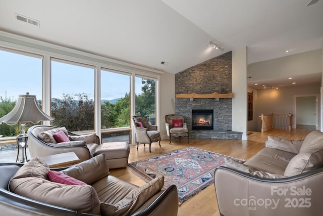 living room with a stone fireplace, high vaulted ceiling, and light hardwood / wood-style floors