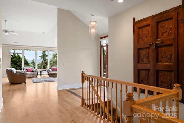 hallway with an inviting chandelier, vaulted ceiling, and light wood-type flooring