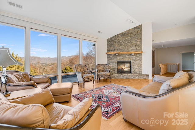 living room with lofted ceiling, a mountain view, a stone fireplace, and light hardwood / wood-style floors