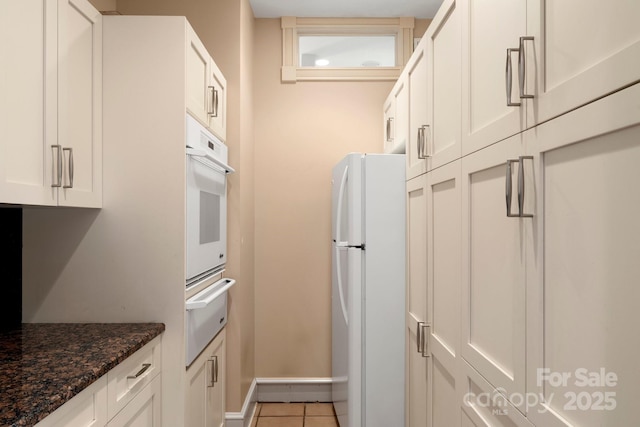 kitchen with white fridge, light tile patterned floors, white cabinets, and dark stone counters