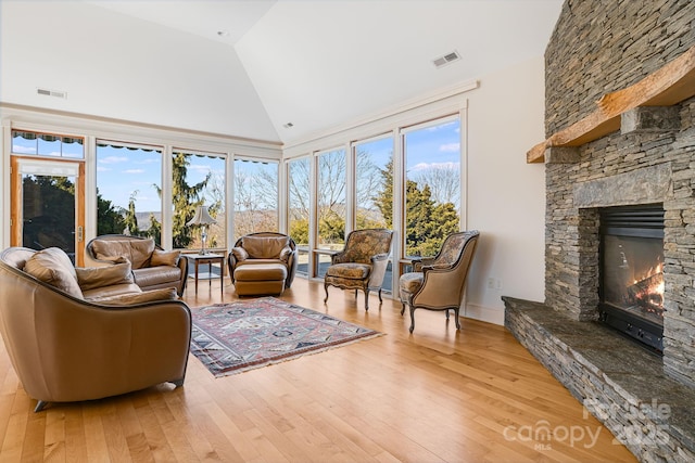 living room featuring plenty of natural light, a stone fireplace, high vaulted ceiling, and light wood-type flooring