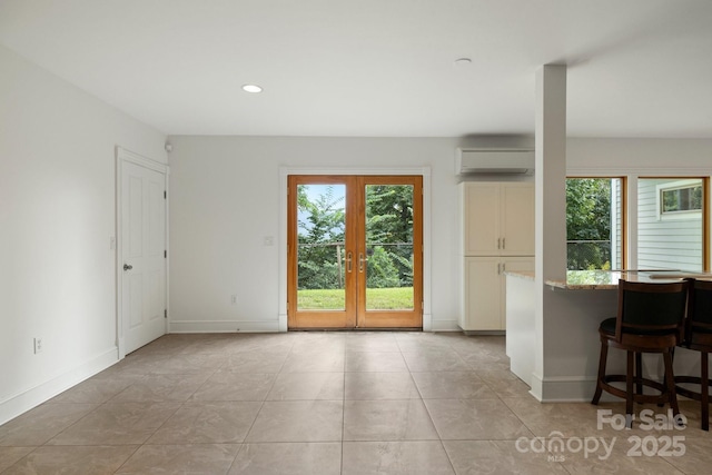 interior space featuring french doors, light stone counters, a wall mounted air conditioner, light tile patterned floors, and a kitchen breakfast bar