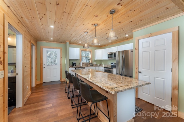 kitchen with decorative light fixtures, a center island, appliances with stainless steel finishes, light stone countertops, and white cabinets