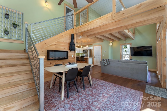 dining room featuring a towering ceiling, ceiling fan, stairway, wood finished floors, and beam ceiling