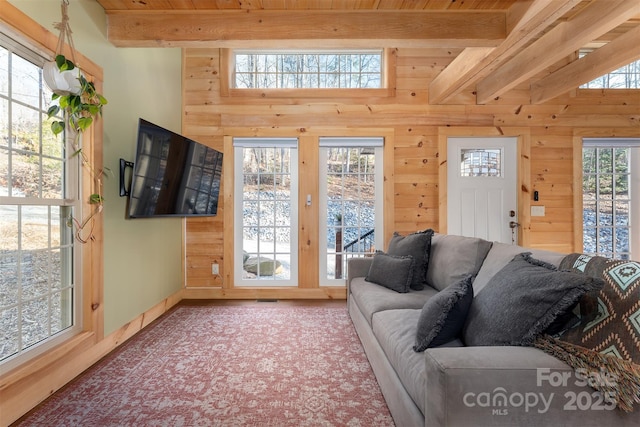 carpeted living room featuring beamed ceiling, wood walls, and baseboards