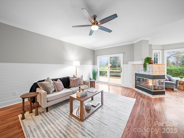 living room featuring a tile fireplace, ornamental molding, hardwood / wood-style floors, and ceiling fan