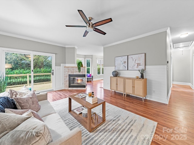 living room with a tile fireplace, crown molding, ceiling fan, and light wood-type flooring