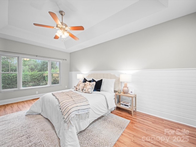 bedroom featuring a tray ceiling, ceiling fan, and light wood-type flooring