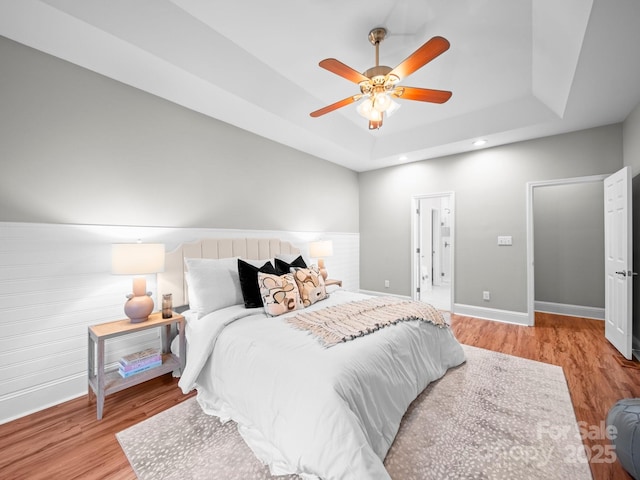 bedroom with ceiling fan, a tray ceiling, and light hardwood / wood-style floors