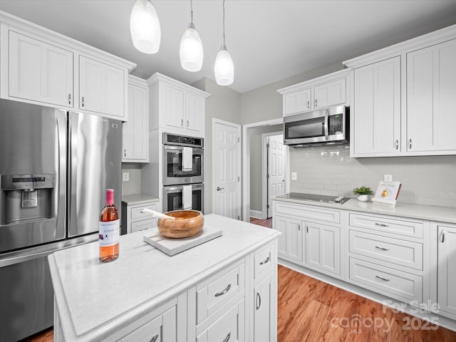 kitchen with appliances with stainless steel finishes, pendant lighting, white cabinetry, decorative backsplash, and light hardwood / wood-style flooring