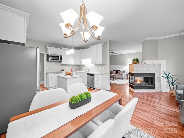 dining room featuring a tile fireplace, sink, light wood-type flooring, ornamental molding, and an inviting chandelier