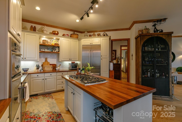 kitchen with butcher block counters, white cabinetry, crown molding, a center island, and appliances with stainless steel finishes