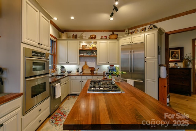 kitchen featuring butcher block countertops, sink, appliances with stainless steel finishes, white cabinetry, and backsplash