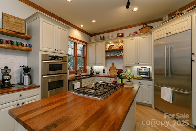 kitchen featuring wood counters, crown molding, stainless steel appliances, decorative backsplash, and white cabinets