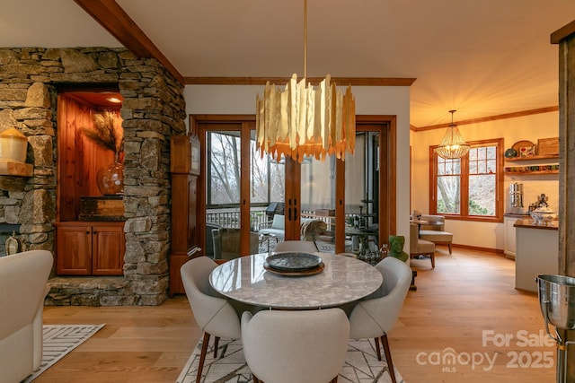 dining area with crown molding, an inviting chandelier, a fireplace, light hardwood / wood-style floors, and french doors