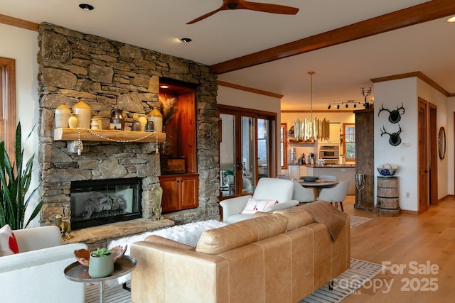 living room with a stone fireplace, beamed ceiling, light hardwood / wood-style flooring, crown molding, and french doors