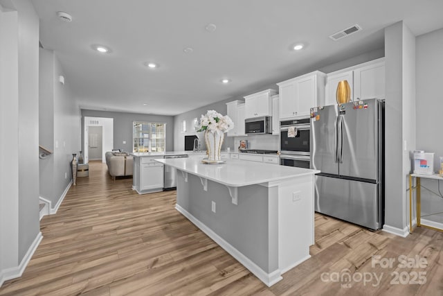 kitchen featuring a breakfast bar, a center island, appliances with stainless steel finishes, light hardwood / wood-style floors, and white cabinets