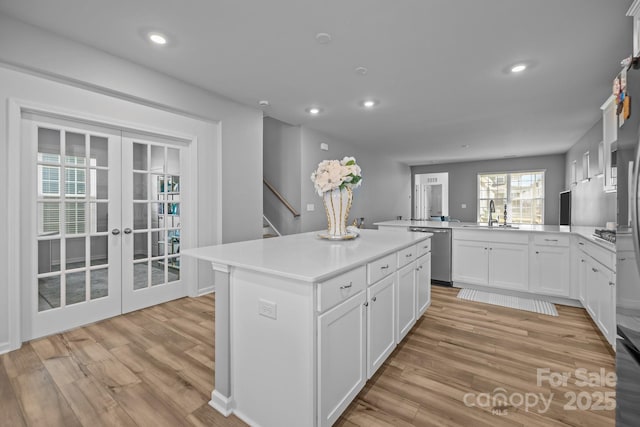 kitchen with a center island, light hardwood / wood-style floors, white cabinets, stainless steel dishwasher, and kitchen peninsula