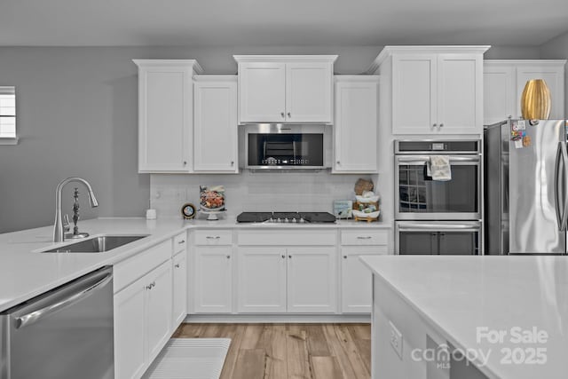 kitchen featuring appliances with stainless steel finishes, white cabinetry, sink, decorative backsplash, and light hardwood / wood-style flooring