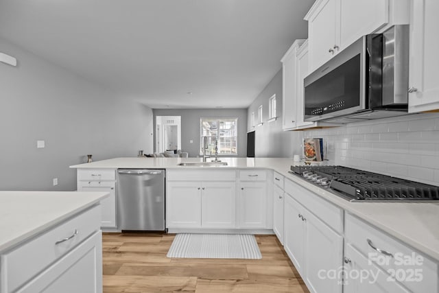 kitchen with sink, light hardwood / wood-style flooring, white cabinetry, stainless steel appliances, and kitchen peninsula