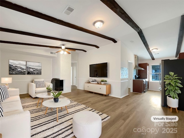 living room with beamed ceiling, ceiling fan, and light wood-type flooring