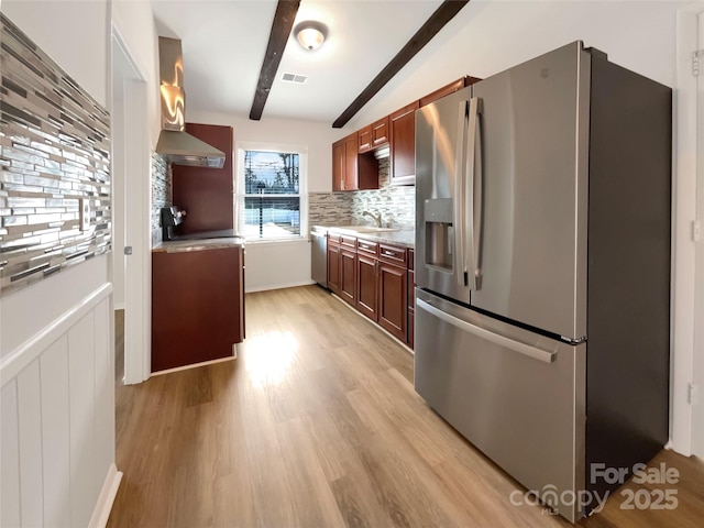 kitchen featuring sink, beam ceiling, stainless steel appliances, tasteful backsplash, and light wood-type flooring