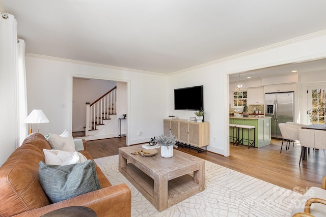 living room featuring light wood-style flooring, crown molding, and stairway