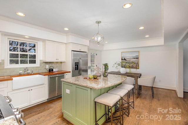 kitchen featuring decorative light fixtures, appliances with stainless steel finishes, white cabinetry, a kitchen island, and a sink