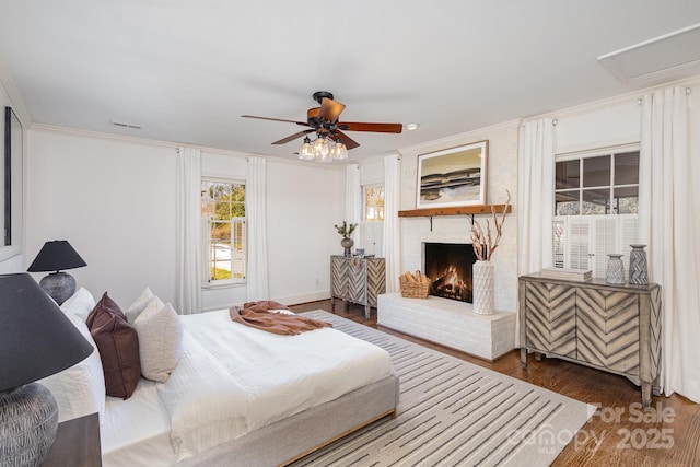 bedroom featuring visible vents, a ceiling fan, ornamental molding, dark wood-style flooring, and a brick fireplace