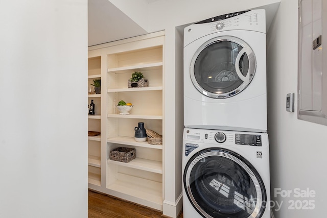 laundry area featuring dark wood-type flooring, stacked washer / drying machine, laundry area, and electric panel